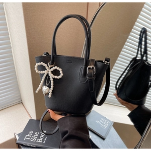 Detail of black pebbled leather bucket bag with pearl bow and silver heart pendant