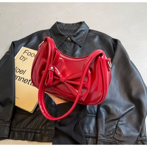 Detail of red glossy shoulder bag with large decorative bow and silver zipper closure