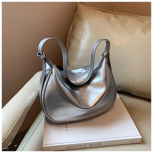 Detailaufnahme einer silbernen Hobo-Bag aus Metallic-Leder auf einem Buch mit weichem Licht