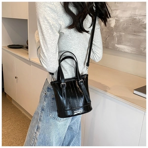 Detail shot of a black glossy bucket bag featuring vertical stitching and leather straps