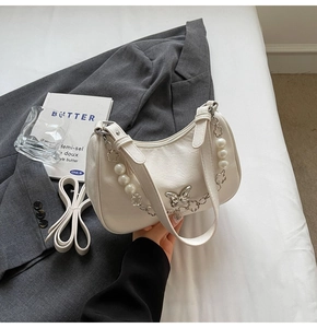Detail of white hobo bag with silver butterfly buckle and decorative pearl chain
