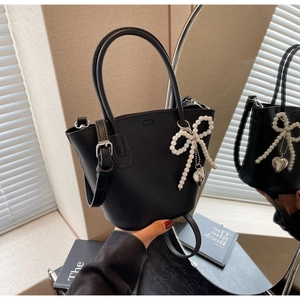 Detail of black pebbled leather bucket bag with pearl bow charm and mirror reflection
