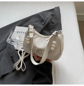Detail of white PU leather bag with silver butterfly charm and pearl chain accent