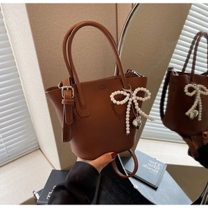 Detail of dark brown pebble leather bucket bag featuring a pearl bow and heart charm