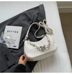 Detail of cream white half-moon bag featuring pearl chain and silver butterfly charm