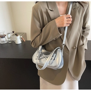 Close-up of a metallic silver half-moon handbag featuring a large bow and chain strap