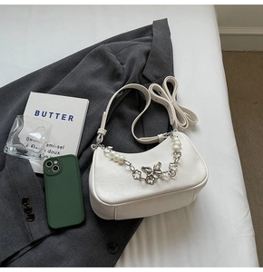Detail of white half-moon bag featuring a metal butterfly charm and pearl chain