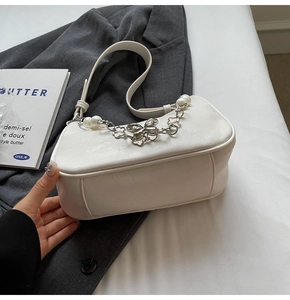 Detail of white leather crescent bag featuring a pearl butterfly chain and flower charm