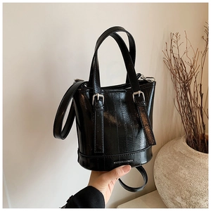 Detail of glossy black bucket bag featuring double handles and a metallic buckle accent