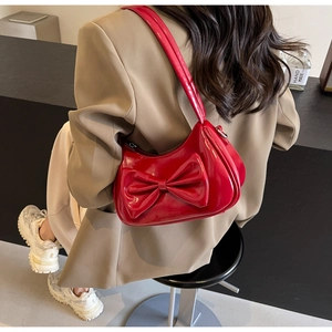 Close-up of bright red patent leather shoulder bag with a large bow worn by a model