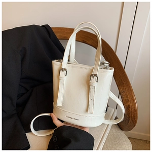 Detail of white bucket bag with vertical texture and silver buckle on wood background