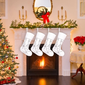Set of four white plush Christmas stockings with silver snowflake embroidery on a fireplace
