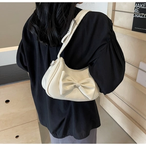 Detail of a cream faux leather underarm bag featuring a large bow and silver buckle strap
