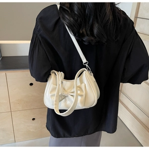 Detail of a creamy beige bow shoulder bag with glossy leather and slim crossbody strap