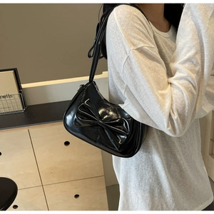 Detail of black patent leather shoulder bag with a large decorative bow and shiny finish