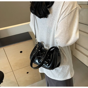 Detail view of a black glossy shoulder bag with a large bow showing on the model