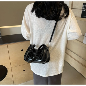 Detailed view of black patent leather bag with a large bow and slim shoulder strap