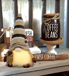 Close-up of lighted coffee gnome with knitted hat and tiny burlap sack of coffee beans