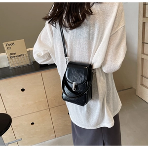 Détail du sac à téléphone en cuir verni noir brillant avec un fermoir en métal argenté