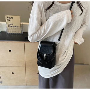 Mini sac bandoulière en cuir verni noir avec boucle argentée porté par un modèle