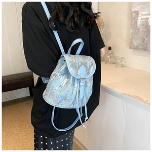 Détail d'un mini sac à dos à paillettes bleu clair avec cordon et rabat en cuir sur modèle