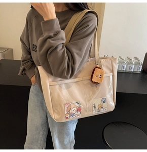 Detail of beige nylon tote bag featuring a clear PVC front pocket and cute plush biscuit charm