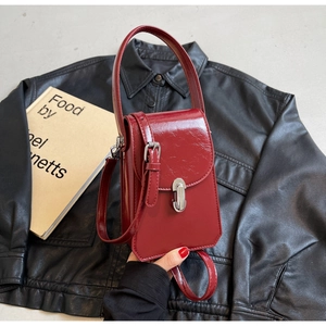 Détail du mini sac bordeaux en cuir brillant avec boucle argentée sur veste noire