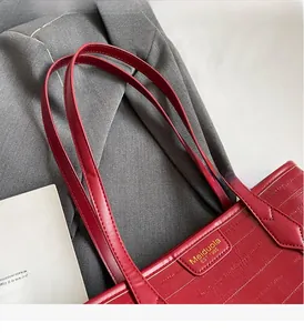 Close-up of red leather tote bag showing reinforced handles and gold Meiduola logo