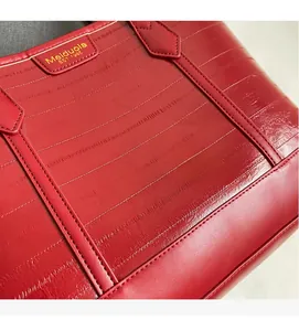 Detail of red tote bag featuring textured leather surface and gold brand name plate