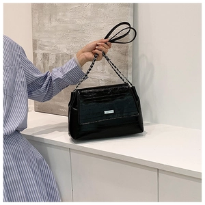 Detail of black faux leather tote with silver chain strap and subtle logo plaque