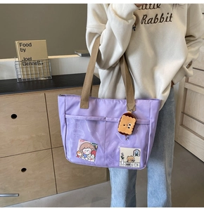 Detail of purple nylon tote bag with transparent pocket and plush biscuit keychain charm