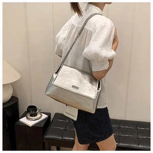 Silver metallic flap shoulder bag with chain strap shown in a lifestyle commuter setting