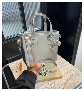 Detail of silver metallic tote bag with logo and silver teddy bear charm on marble