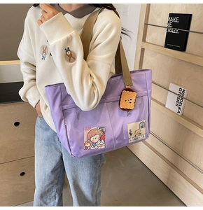Detail of purple nylon tote bag with transparent PVC pockets and plush biscuit pendant