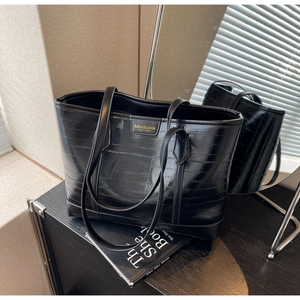 Close-up of black textured tote bag featuring gold Meiduola logo and slim shoulder straps