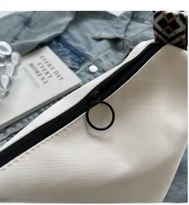 Detail of smooth black zipper and round metal pull on a beige canvas crossbody bag