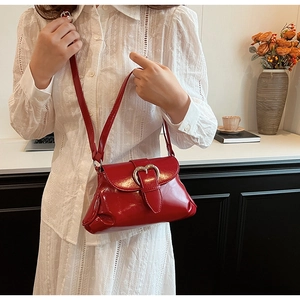 Détail du sac selle en cuir verni rouge avec boucle cœur sur une tenue en dentelle