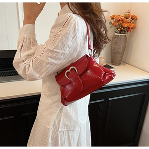 Detail of red patent leather shoulder bag with a large silver heart-shaped metal buckle