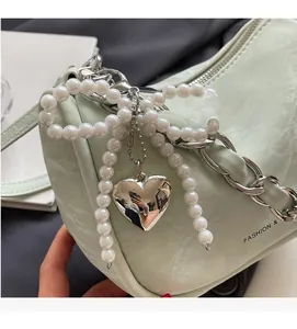 Detail of pale green handbag featuring a pearl bow charm and silver heart pendant