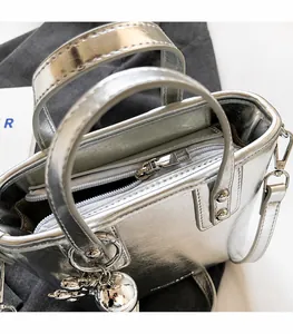 Detail of a silver metallic handbag featuring a smooth zipper and spherical charm