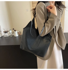 Detail of black woven tote bag with slim leather straps in a minimalist lifestyle setting