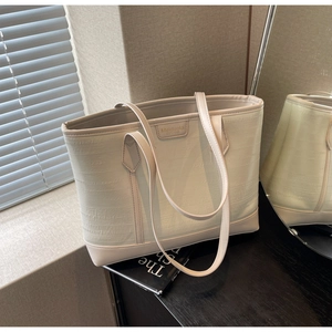 Detail of cream tote bag featuring textured grain surface and metallic brand plaque