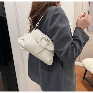 Detail of cream white patent leather shoulder bag with silver heart buckle and side pleats