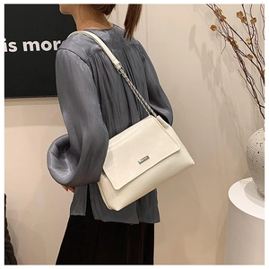 Detail of white faux leather shoulder bag with chain strap and metallic logo on model
