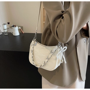 Detail of cream white shoulder bag with silver chain and beaded bow charm in a cafe setting