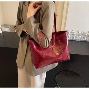 Macro view of dark red tote bag featuring glossy horizontal embossing and dual straps