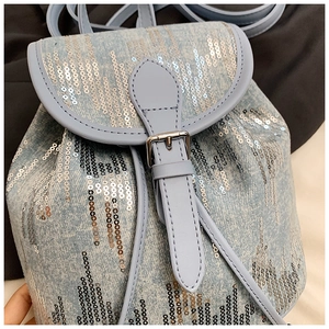 Détail d'un sac à dos en denim bleu clair avec des paillettes et boucle argentée
