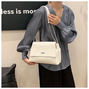 Detail of cream white faux leather shoulder bag with silver chain strap on a model
