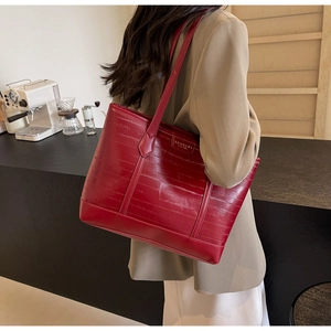 Close-up of a burgundy tote bag with horizontal texture and metal brand plate