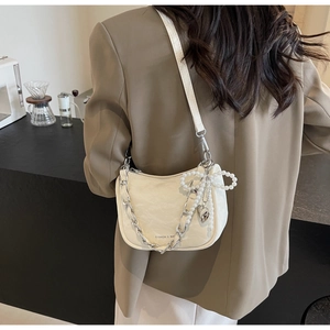 Detail of beige textured leather bag with pearl bow and metal heart charm accessories